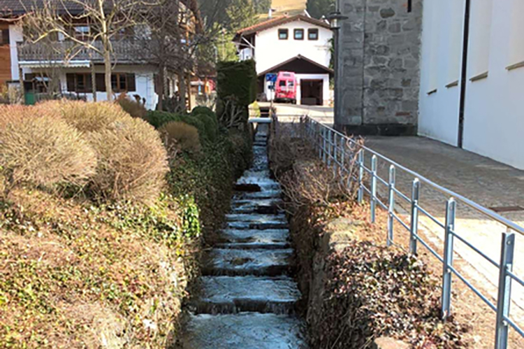 Bestehendes Gerinne am Burgberger Dorfbach entlang der Kirche. Auf den hier sichtbaren Abflussquerschnitt soll der Burgberger Dorfbach auch im Oberlauf verbreitert werden, um künftig hundertjährliche Hochwasserereignisse ohne Ausuferungen abführen zu können. Bestehendes Gerinne am Burgberger Dorfbach entlang der Kirche.